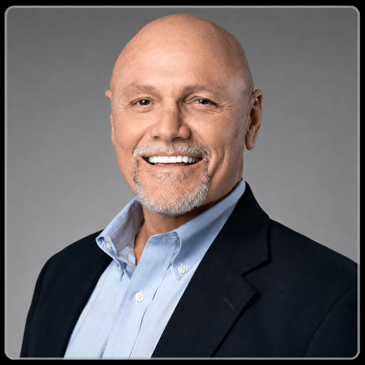 Bald man smiling in blue shirt and dark blazer, looking confidently at the viewer.
